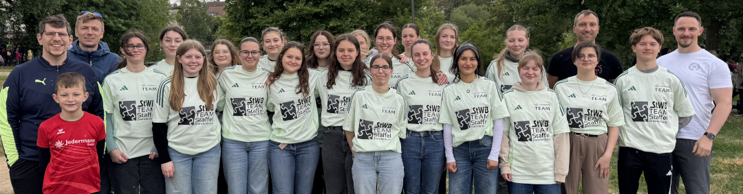 Mannschaftsfoto der Teilnehmenden des Staffellaufs. Zu sehen sind 4 Lehrer der Schule als Läufer und 20 Schülerinnen und Schüler der Jahrgangsstufe 11 in ihren Streckenposten-Shirts